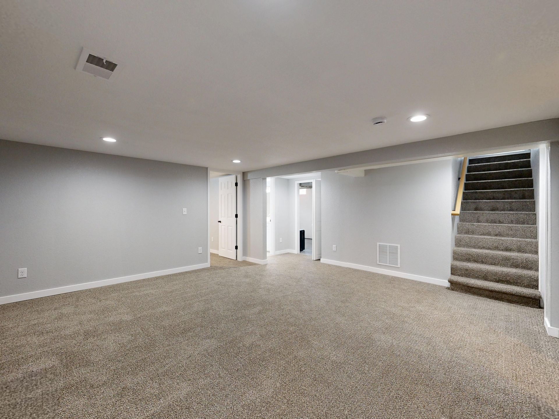 Empty modern basement with beige carpet and white walls, ideal for renovation.